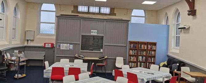 a room in an old methodist church with tables and red and white chairs