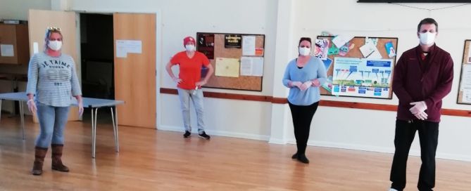 Four people in face masks standing metres away from each other