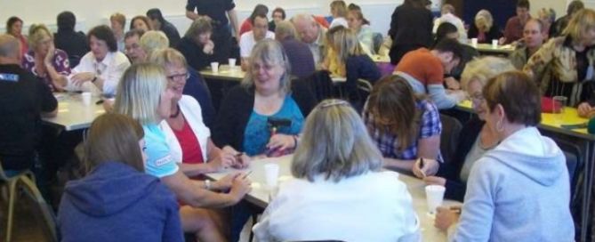 a room of people sat a round tables listening to each other